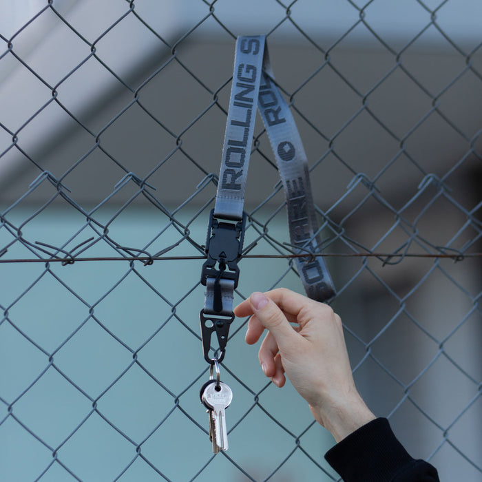 Rolling Square Lanyard - Digital ID & QR Lost Mode - Silver Fog - Silver fog Rolling Square lanyard with black clip holding a silver key against a chain-link fence background. - Rolling Square
