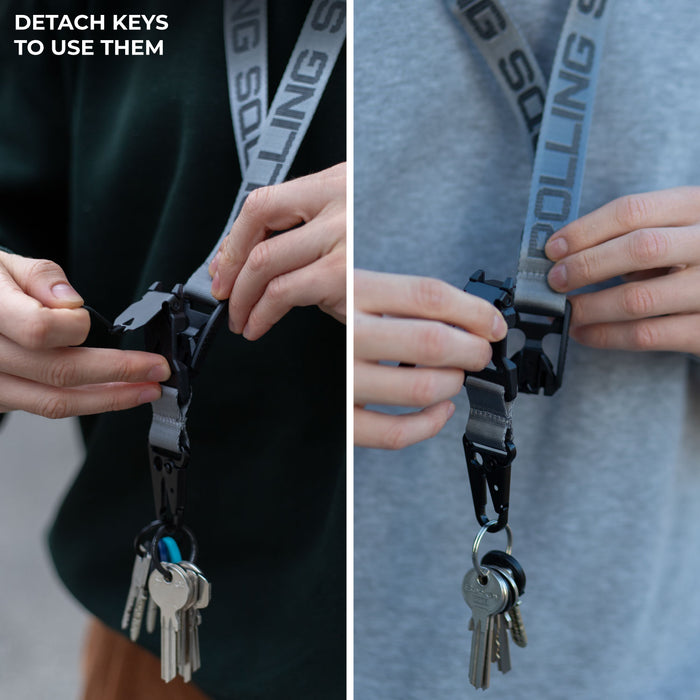 Rolling Square Lanyard - Digital ID & QR Lost Mode - Silver Fog - Two hands detaching black Rolling Square lanyard with white logo and keys attached, shown on gray and dark green shirts. - Rolling Square