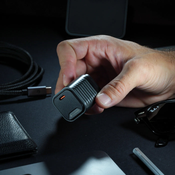 Supertiny 65W + Free 2in1 Cable (Bundle) - US - Compact black 65W charger with USB-C port held in hand over dark surface with cables and accessories. - Rolling Square