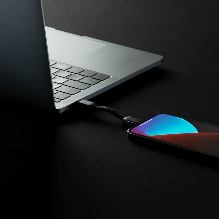 inCharge® Mini - The Smallest cable ever - USB to Lightning - Compact black charging cable connected between a sleek silver laptop and a smartphone with a vibrant blue and red gradient. - Rolling Square