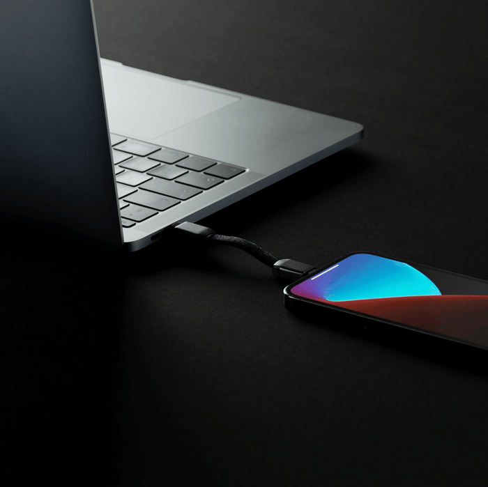 inCharge® Mini - The Smallest cable ever - USB to Lightning - Compact black charging cable connected between a sleek silver laptop and a smartphone with a vibrant blue and red gradient. - Rolling Square