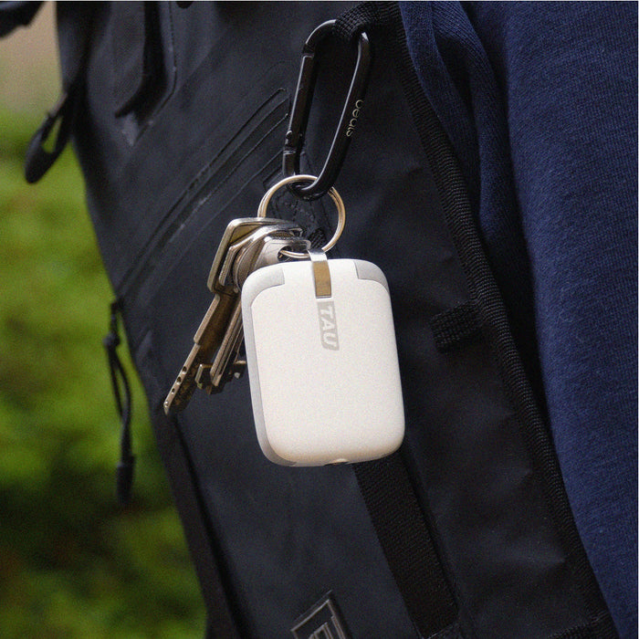 TAU® - Always-charged power bank - Charcoal Black - Compact white power bank with rounded edges attached to black backpack by carabiner clip alongside several keys. - Rolling Square