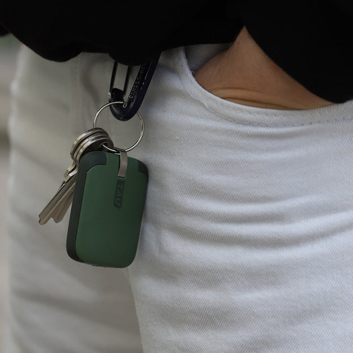 TAU® - Always-charged power bank - Charcoal Black - Compact agave green power bank attached to keyring held against white shirt. - Rolling Square